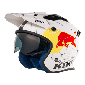 Der Mission Kini KINI RED BULL XDR 1.0 Helm ist ein weißer Motocross-Helm mit sechseckigem Muster, schwarzem Visier, blauer Innenpolsterung und großem roten und gelben Red Bull Logo. Der Schriftzug "KINI" ist in Schwarz auf der Seite aufgedruckt.