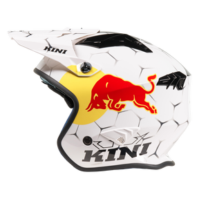 Der Mission Kini KINI RED BULL XDR 1.0 Helm ist ein weißer Motocross-Helm mit einem sechseckigen Muster, einem großen roten Bullen-Logo auf einem gelben Kreis, schwarzem "KINI"-Schriftzug und fetten schwarzen, eckigen Mustern.